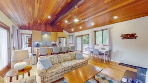 Uma sala espaçosa com teto de madeira, um sofá, uma mesa de centro e um espaço de jantar com cadeiras e uma mesa.