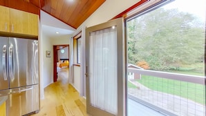 Cozinha moderna com eletrodomésticos de aço inoxidável, teto de madeira e vista para uma varanda com jardim.