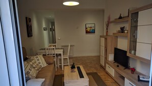 A modern living room with a sofa, coffee table, TV, and a dining area with a table and chairs. - Great Apt near Atocha 3hab 2b (Madrid)