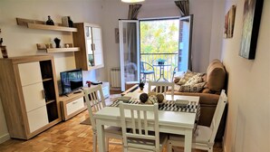 A compact living space with a dining area, kitchenette, and a balcony with a view of trees. - Great Apt near Atocha 3hab 2b (Madrid)