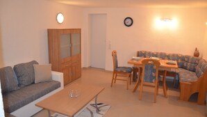 Een woonkamer met een bank, een salontafel, een eettafel met stoelen, een kast en een klok aan de muur.