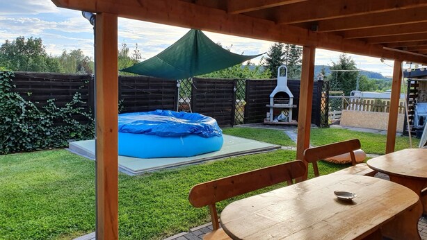 Een houten terras met een tafel, stoelen, een trampoline en een barbecueplek.