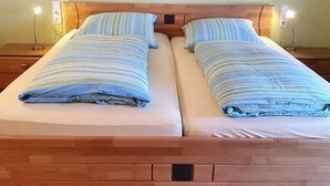 Een tweepersoonsbed met gestreepte beddengoed, een houten hoofdbord en bedlampjes.