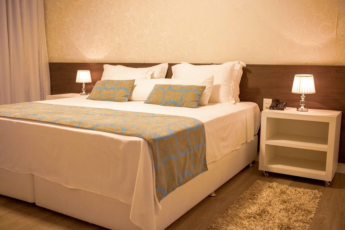 A hotel room with a large bed, two bedside tables, a nightstand, a lamp, and a carpeted floor.