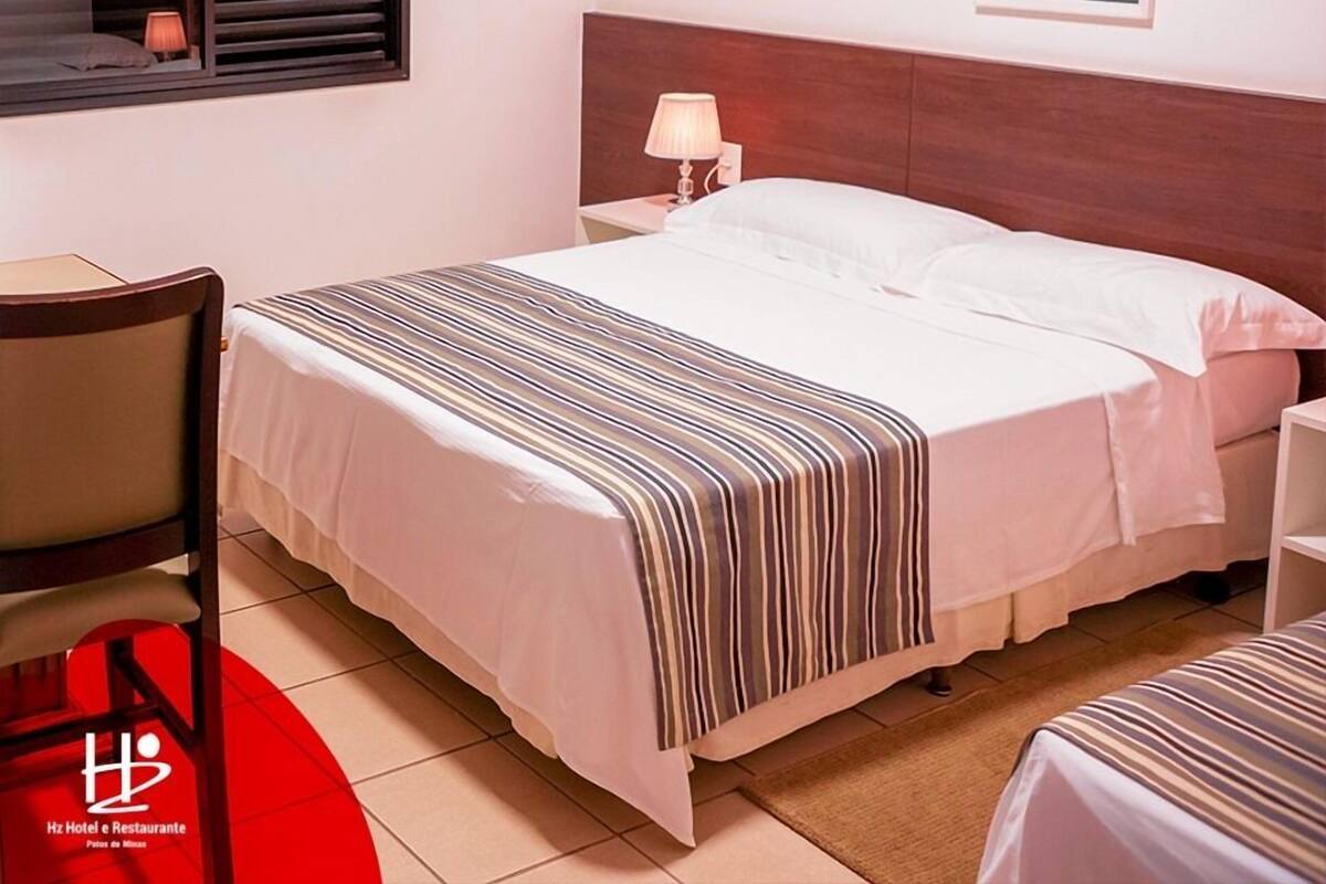 A hotel room with a bed, bedside table, lamp, and a framed picture on the wall.