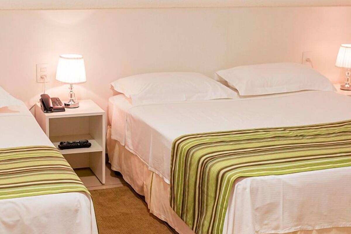 A hotel room with two single beds, each with a bedside table, lamp, and a telephone.