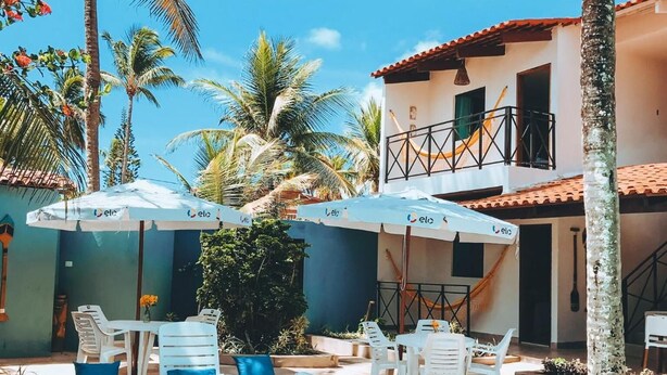 A poolside area with lounge chairs, umbrellas, and a building with a red-tiled roof. - Pousada Oceano (Ipojuca)