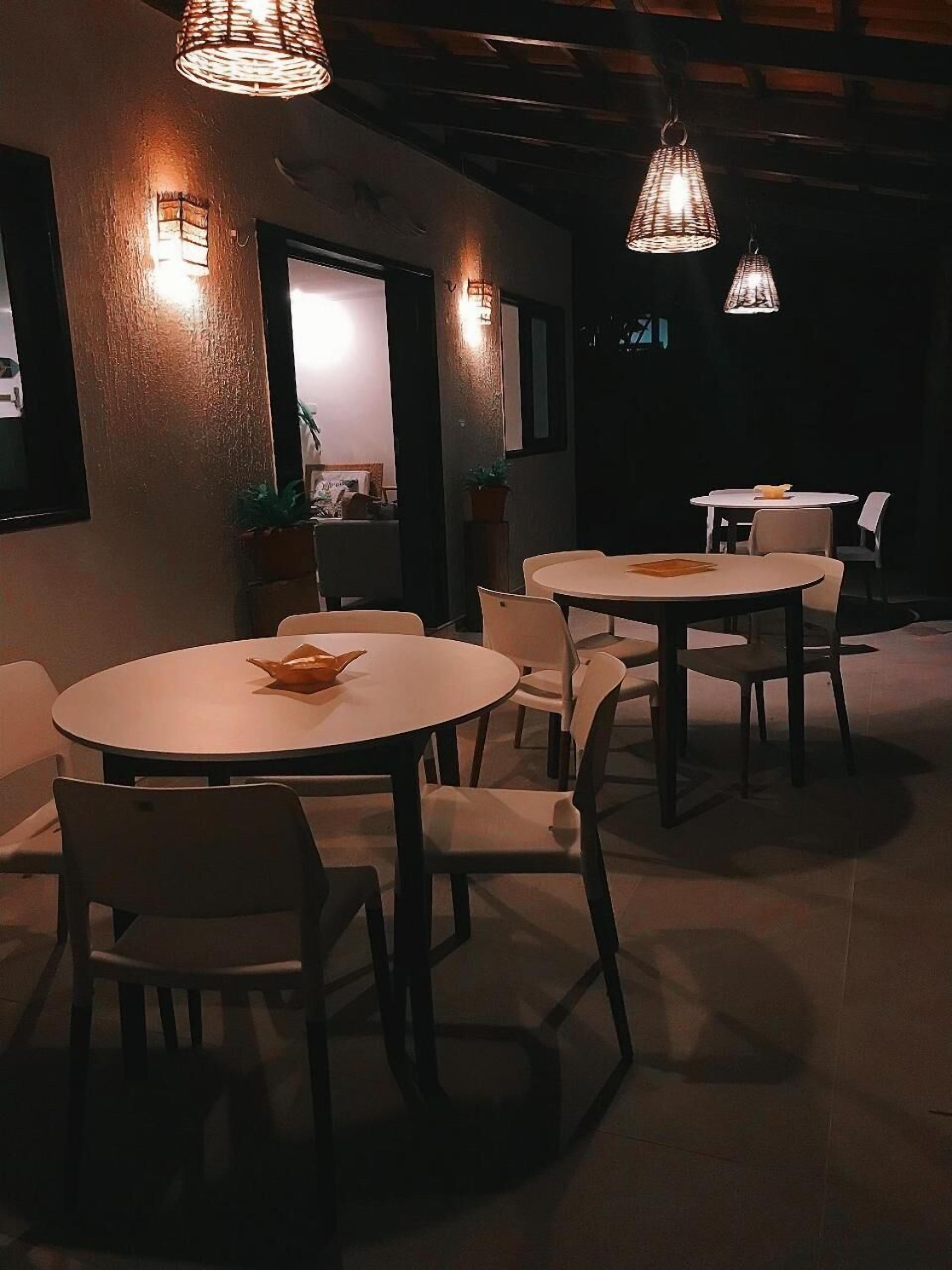 Un comedor tenuemente iluminado con mesas y sillas redondas, techo de madera y luces fijadas en las paredes.