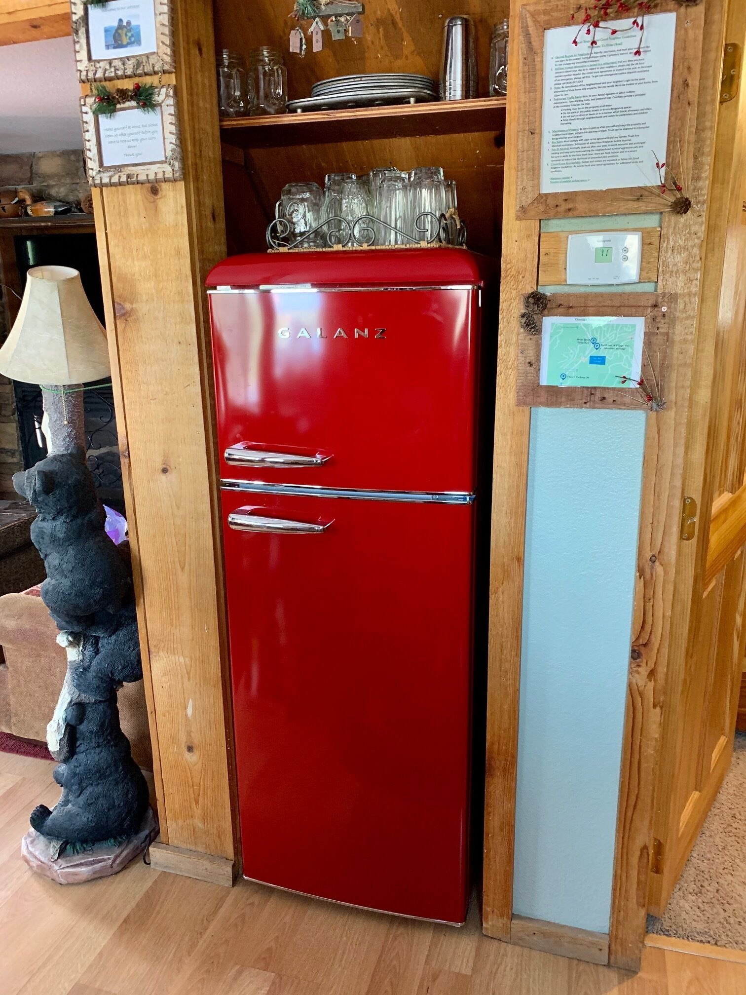 A red Galanz refrigerator in a wooden-paneled room with a small bear statue, a lamp, and various items on shelves.