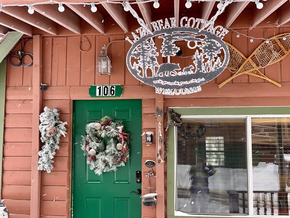 Una puerta verde con un adorno de lazo, un letrero que dice "106" y un letrero de "Bear Cottage" arriba.