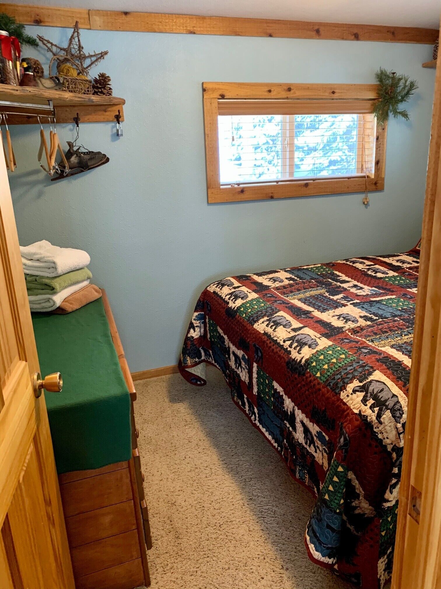 A cozy bedroom with a bed, a window with a view, a shelf with personal items, and a door.