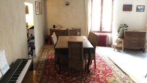Un comedor con un piano, una mesa con sillas, un radiador y un aparador.