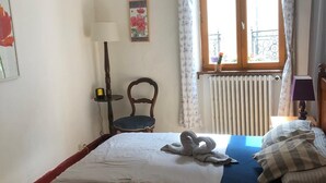 Un dormitorio con cama, una silla, una lámpara, una ventana con cortinas y un radiador.
