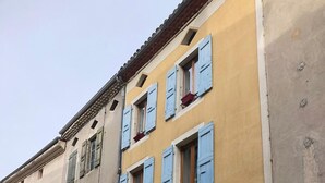 Una hilera de edificios con contraventanas azules, un cartel de no estacionamiento y un árbol pequeño.