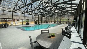 Un espace extérieur abrité avec une piscine, des tables et des chaises, le tout entouré d’une structure en verre.