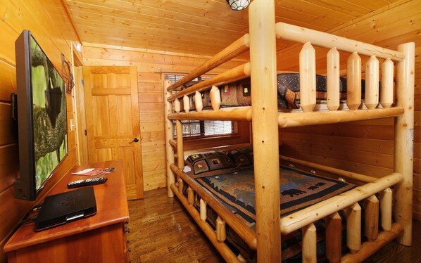 Interior de una cabaña de madera con literas, un televisor y un escritorio con una computadora portátil.