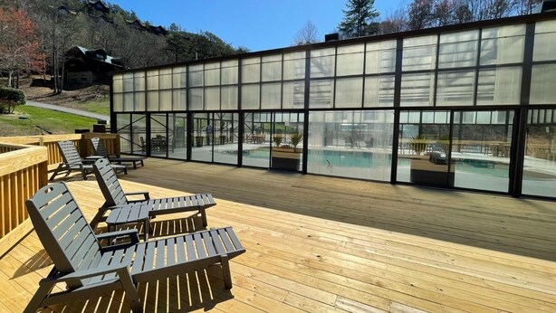 Une terrasse en bois avec des chaises longues et une piscine abritée par une structure en verre.
