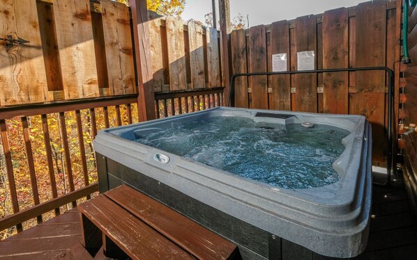 Een hottub in een houten buitenomgeving met een houten hek en een bank.