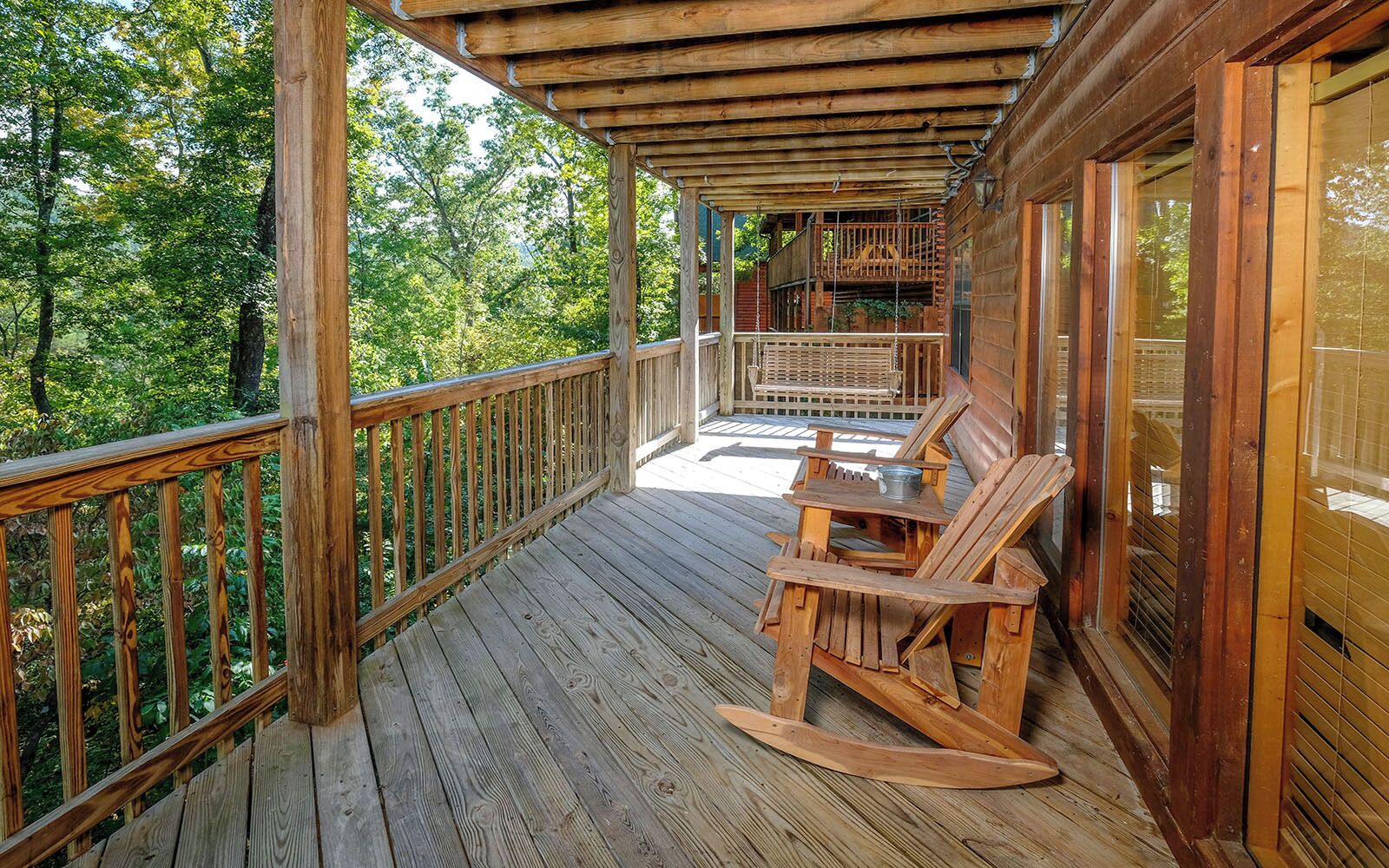 A wooden deck with a rocking chair and a table, surrounded by a wooden railing.