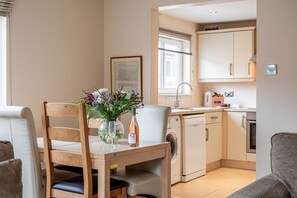 A compact kitchen with a dining area, including a wooden table with a vase of flowers, a washing machine, and a dishwasher.