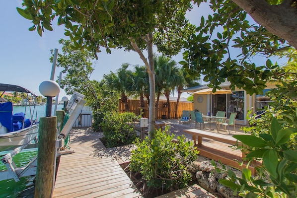 A wooden deck with a boat, outdoor seating, and a fenced area with palm trees.