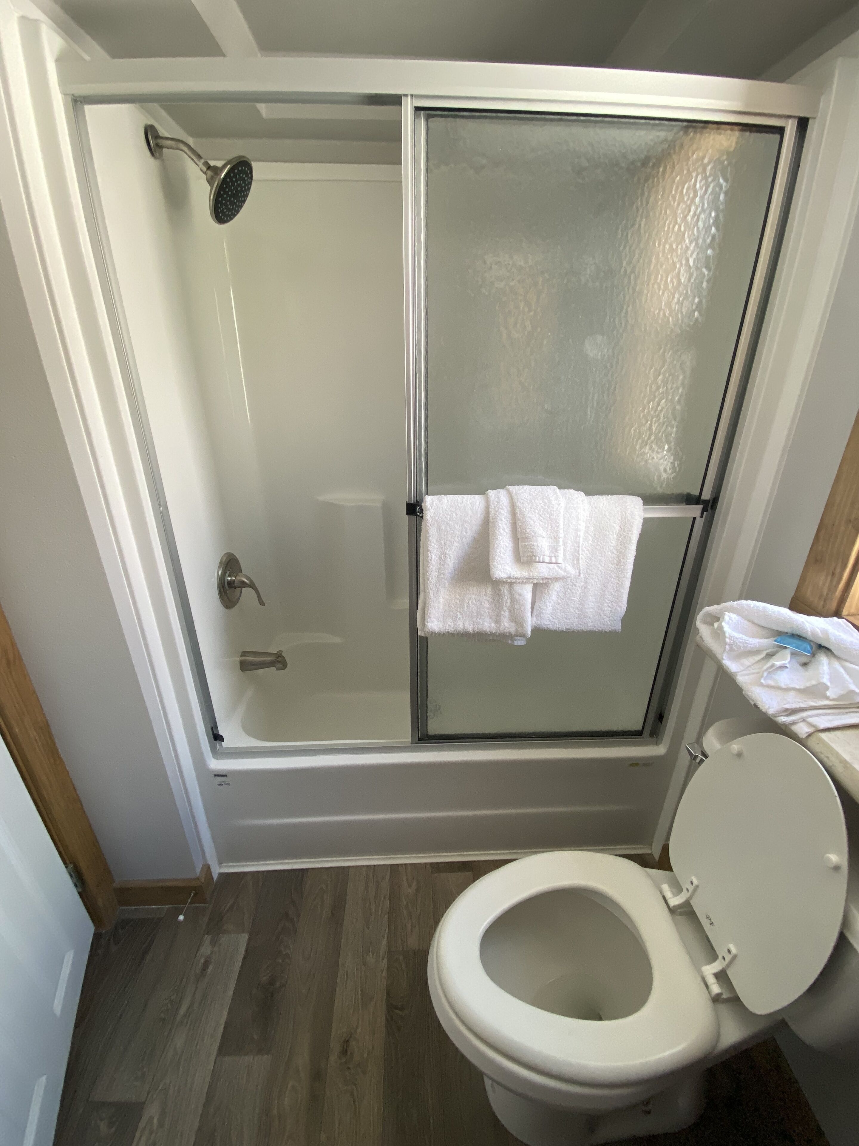Een badkamer met een douchecabine van glas, een toilet en een witte handdoek die aan de douchedeur hangt.