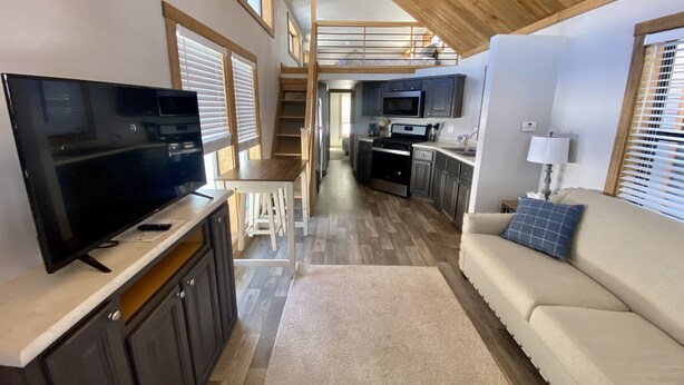 Een compacte, moderne keuken met een centraal eiland, een eetgedeelte met een witte tafel en stoelen, en een gezellige woonruimte met een bank en televisie.