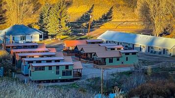 A row of cabins with a central building, surrounded by trees and a hilly landscape.