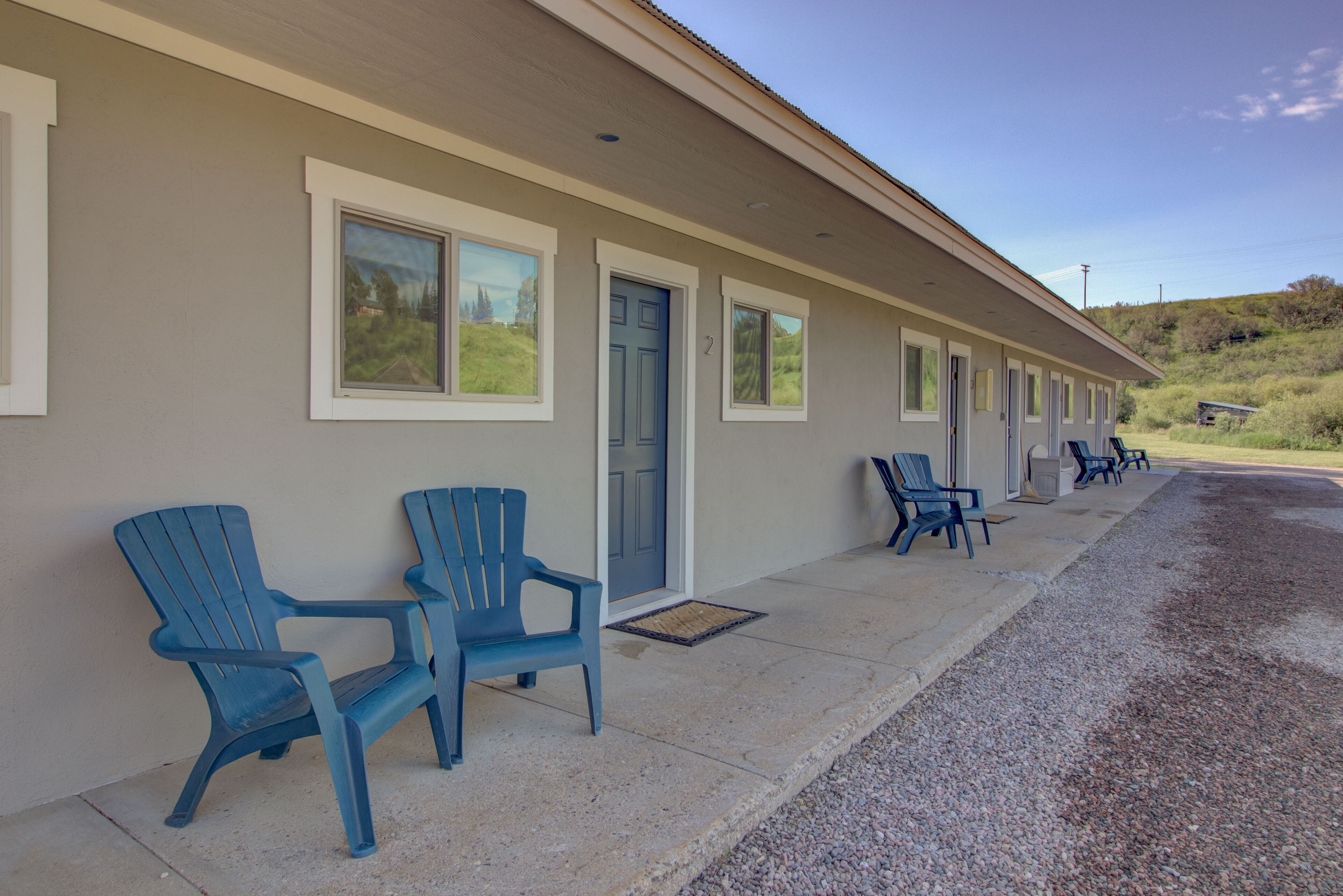 A motel with a row of blue chairs outside, a door, and a number '2' on the wall.