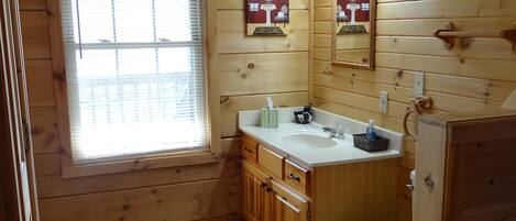 Une salle de bain rustique, située dans une cabane en bois, avec une fenêtre, un lavabo, des toilettes et des placards.