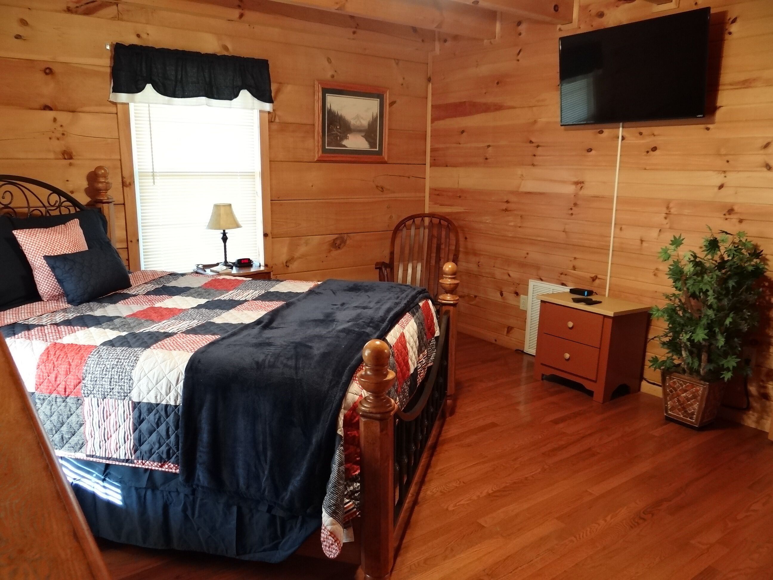 Un dormitorio con paneles de madera, una cama, mesita de noche, lámpara y televisor en la pared.
