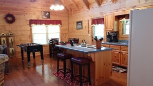 Un intérieur de chalet chaleureux, avec un revêtement en bois, une table de baby-foot, un coin cuisine et un espace repas.