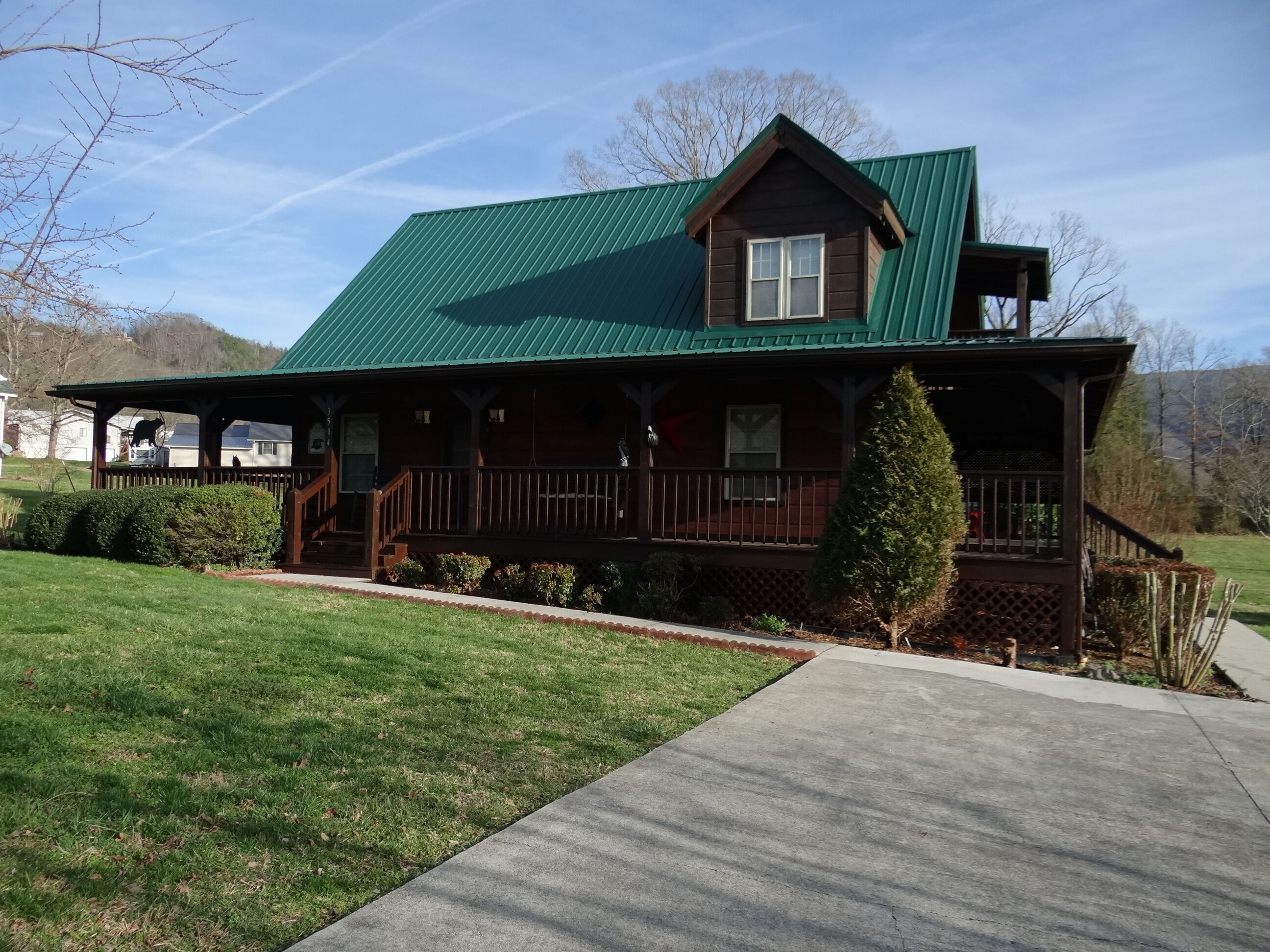 A two-story wooden house with a green roof, a front porch, and a small front yard.