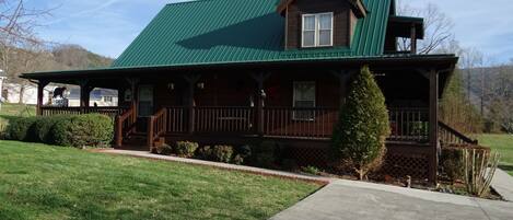 A two-story wooden house with a green roof, a front porch, and a small front yard.
