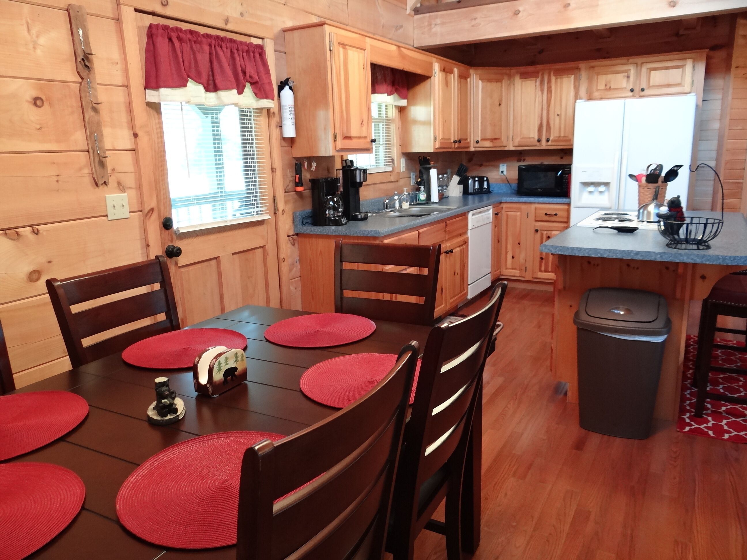 A wooden cabin-style kitchen with a dining table, chairs, and a small refrigerator.
