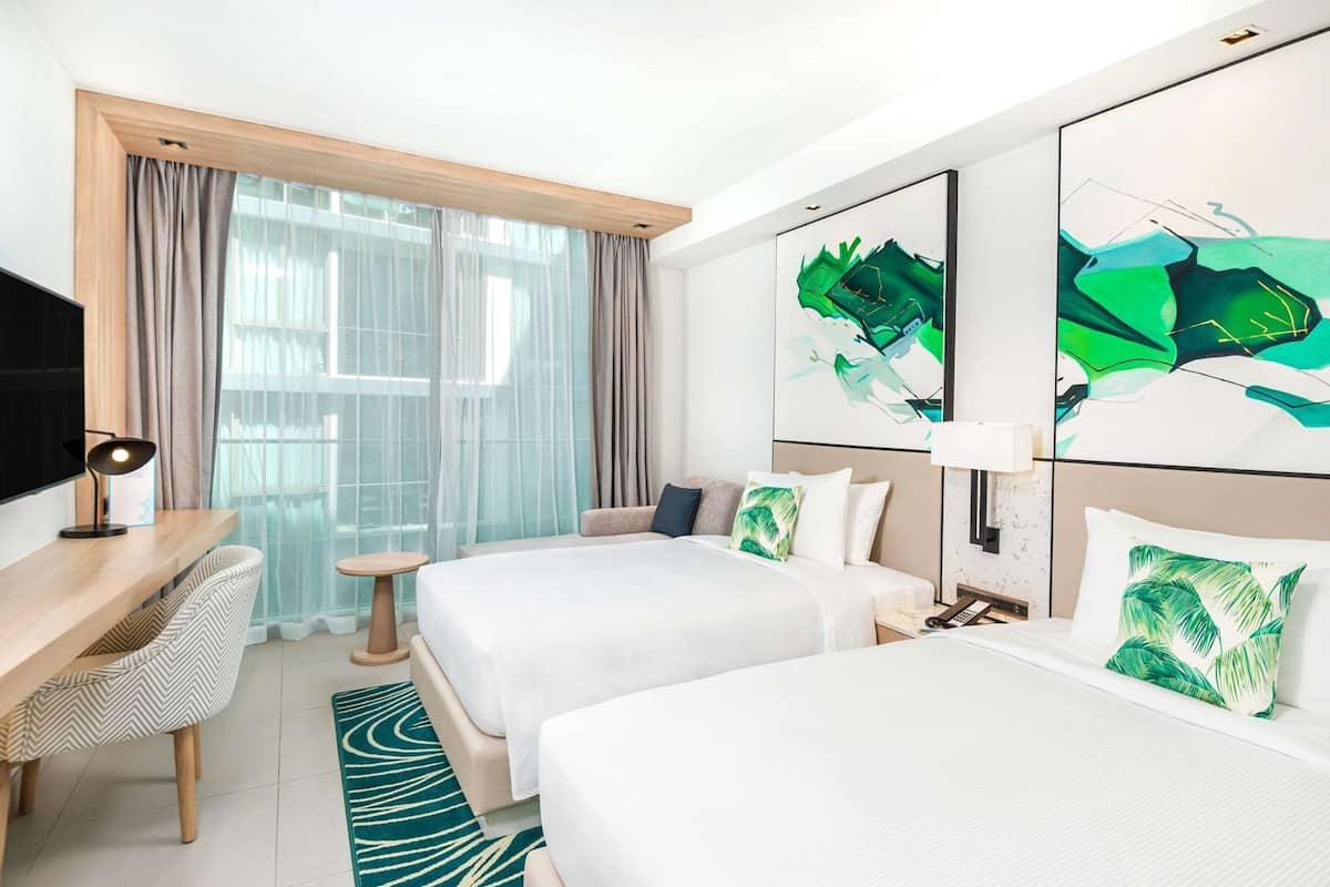 A hotel room with two beds, a desk, a chair, and artwork on the walls.