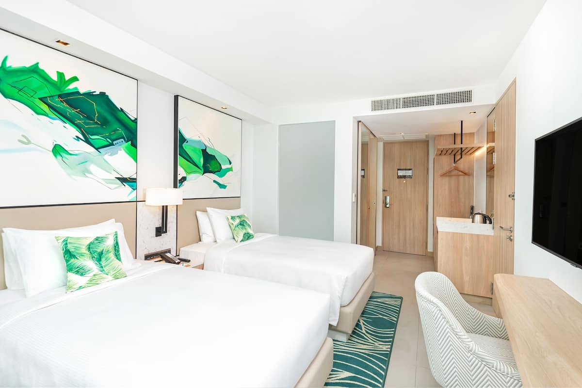 A hotel room with two beds, a desk, a chair, a TV, and artwork on the walls.