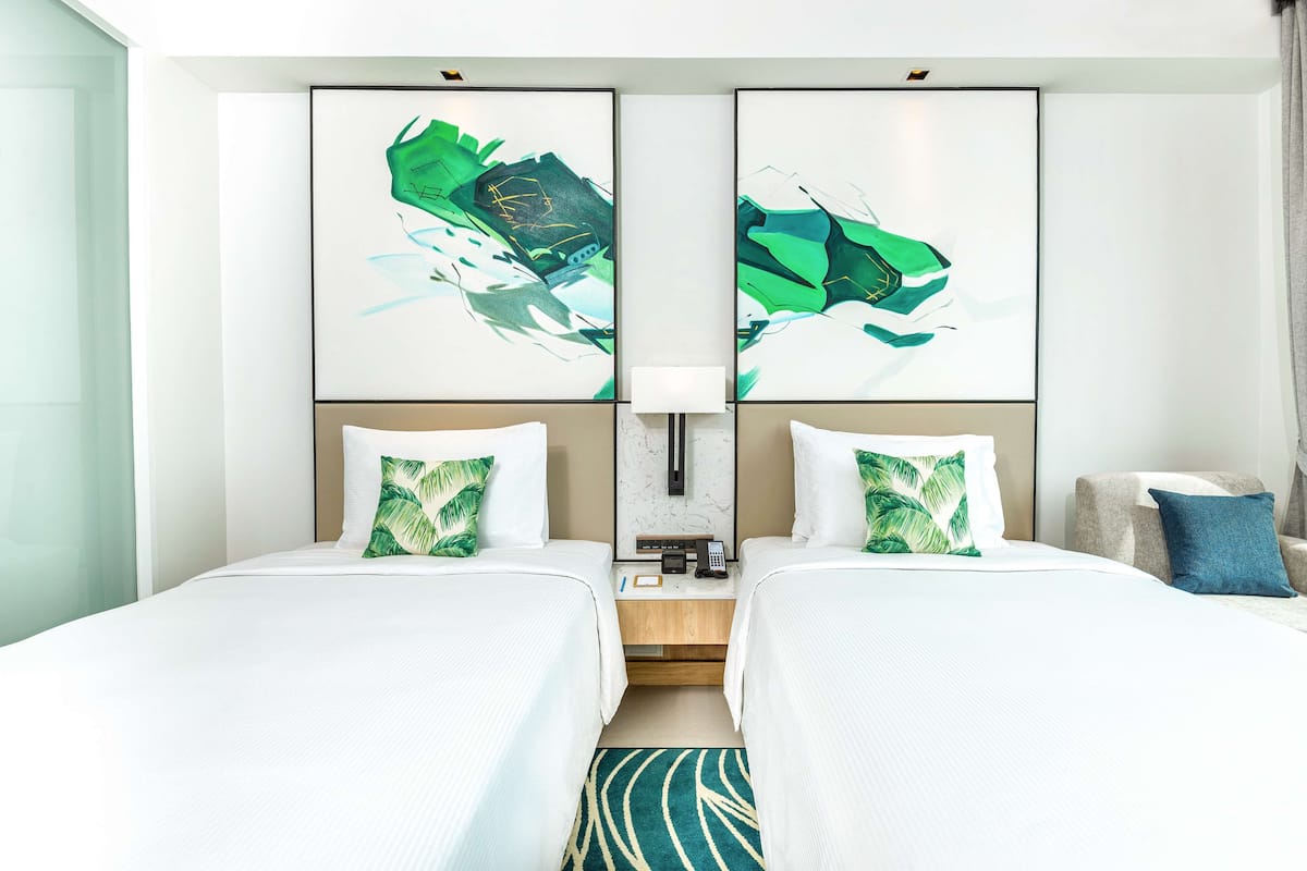 A hotel room with two beds, a nightstand, a lamp, and abstract wall art.