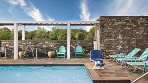 Un área de piscina con sillones de descanso y un muro de piedra.