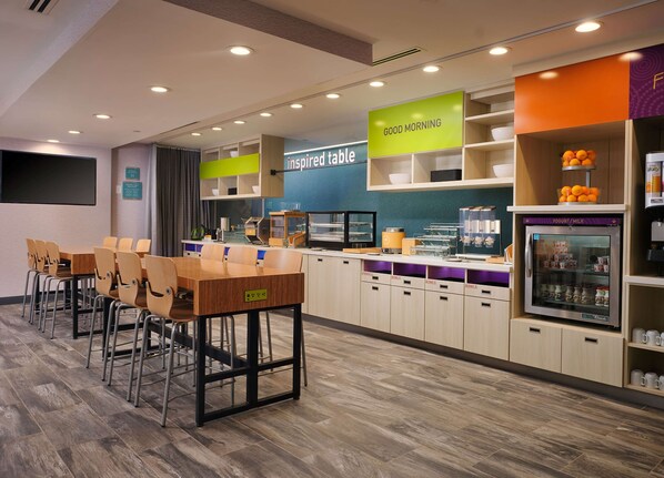 A modern cafe with a wooden table and chairs, a counter with a yogurt/milk dispenser, and a sign that says "inspired table."