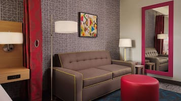 A modern hotel room with a sofa, ottoman, and a large mirror.