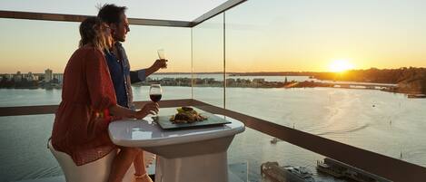 Et par spiser ved et bord med udsigt over byen, et glas vin og en tallerken mad.