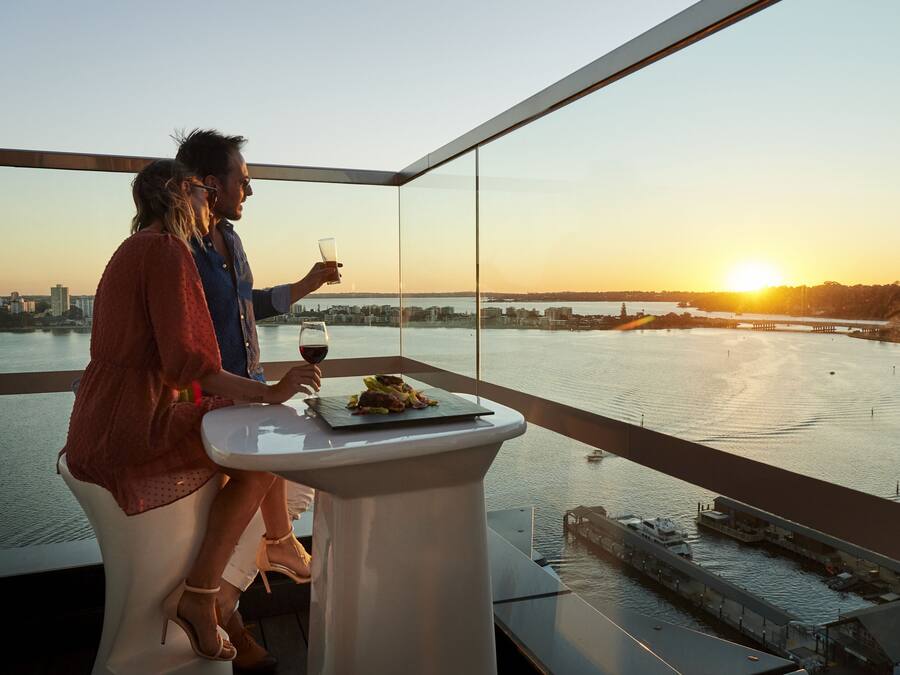 Una pareja cenando en una mesa con vista a la ciudad, una copa de vino y un plato de comida.
