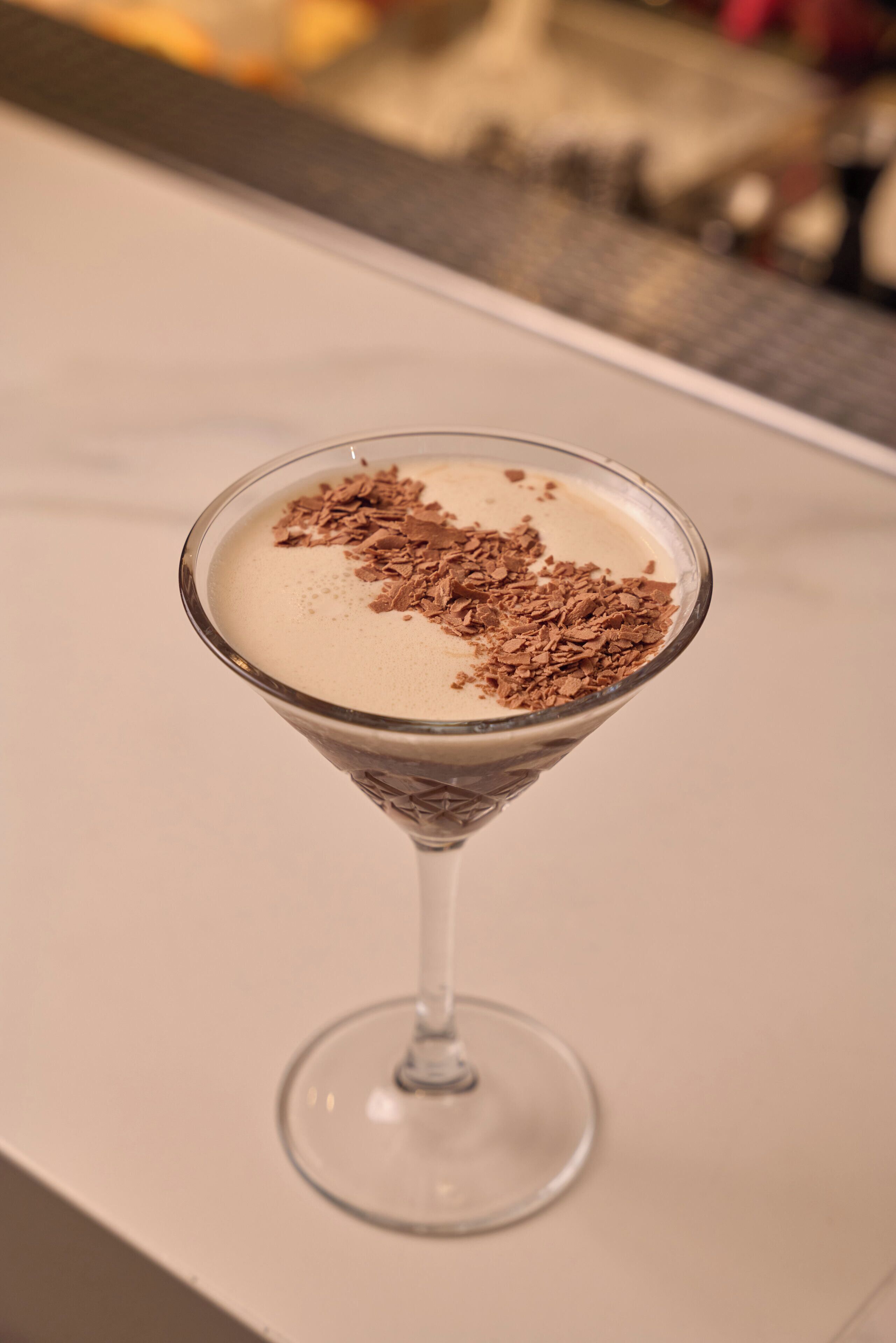 A martini glass with a creamy drink topped with chocolate shavings on a white surface.