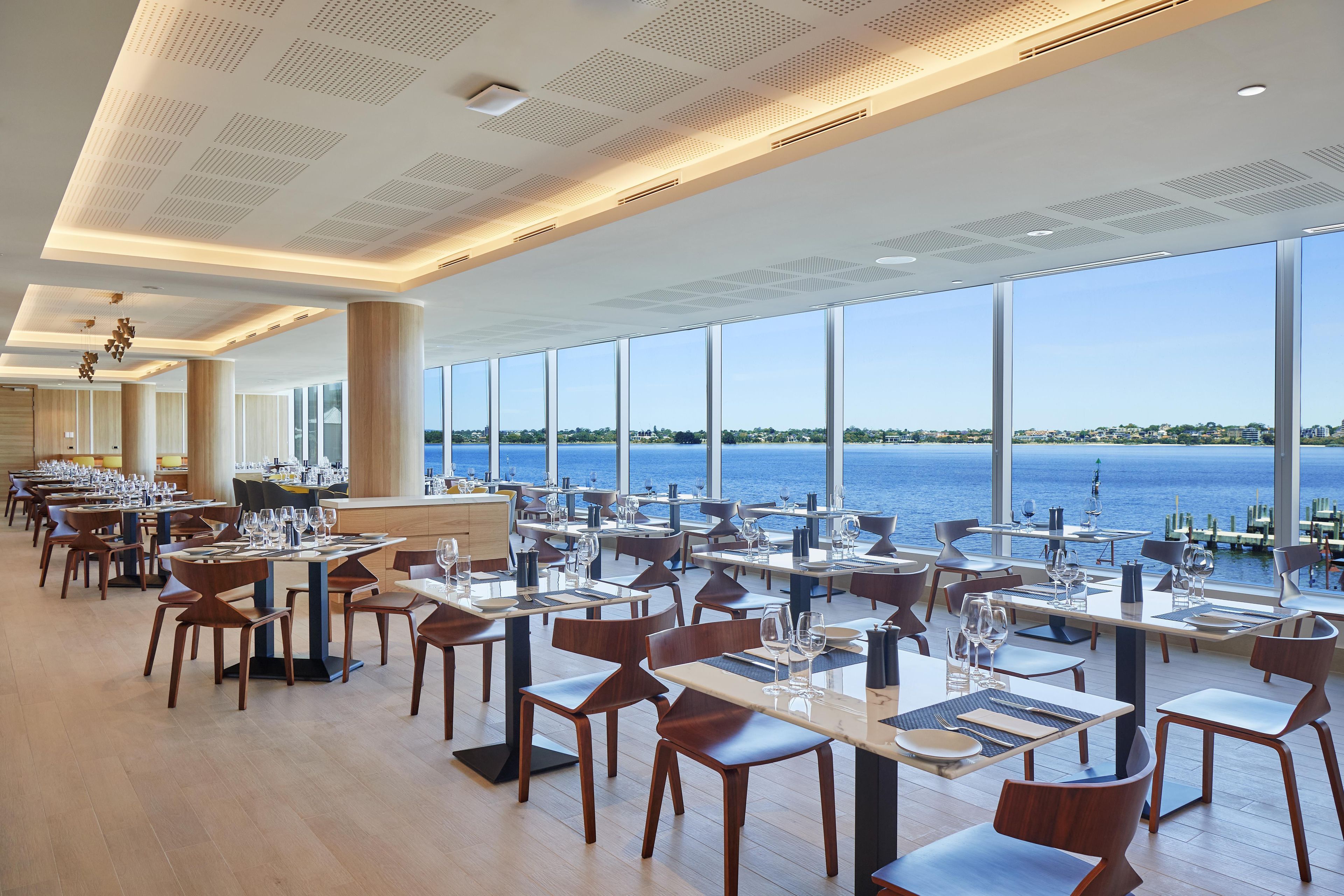 Un restaurant spacieux avec de hauts plafonds, de grandes fenêtres donnant sur la mer et un mobilier moderne.