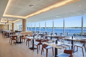 Tilava ravintola, jossa on korkeat katot, suuret ikkunat, joista avautuu näkymä merelle, sekä modernit huonekalut.