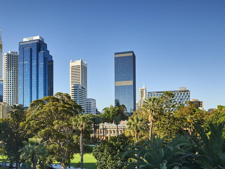A city skyline with modern high-rise buildings, a park with trees, and a clear blue sky.