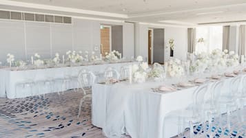 A long banquet table with clear chairs, white tablecloths, and floral centerpieces.