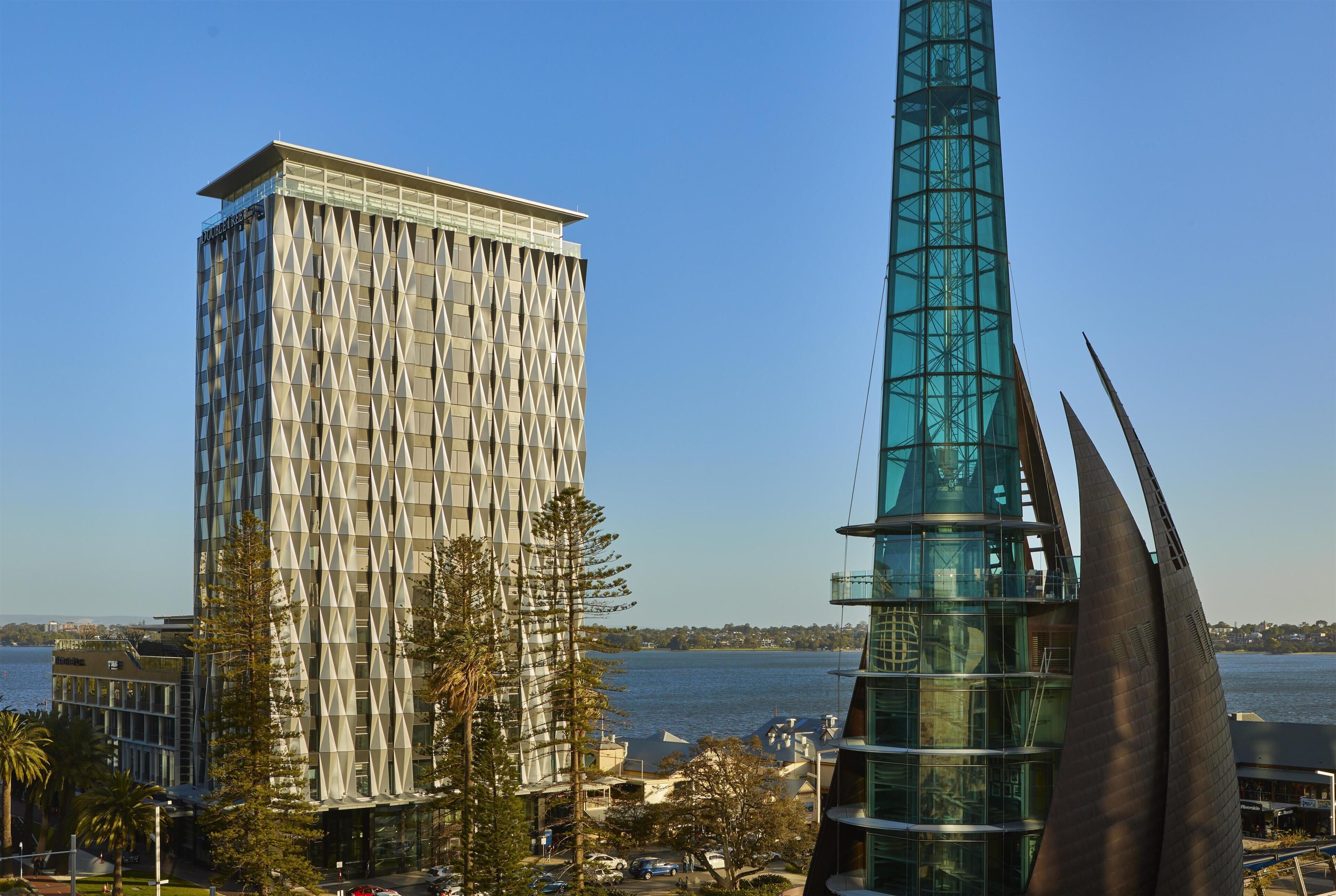 A modern building with a geometric facade, a tall tower with a spiral design, and a waterfront view.