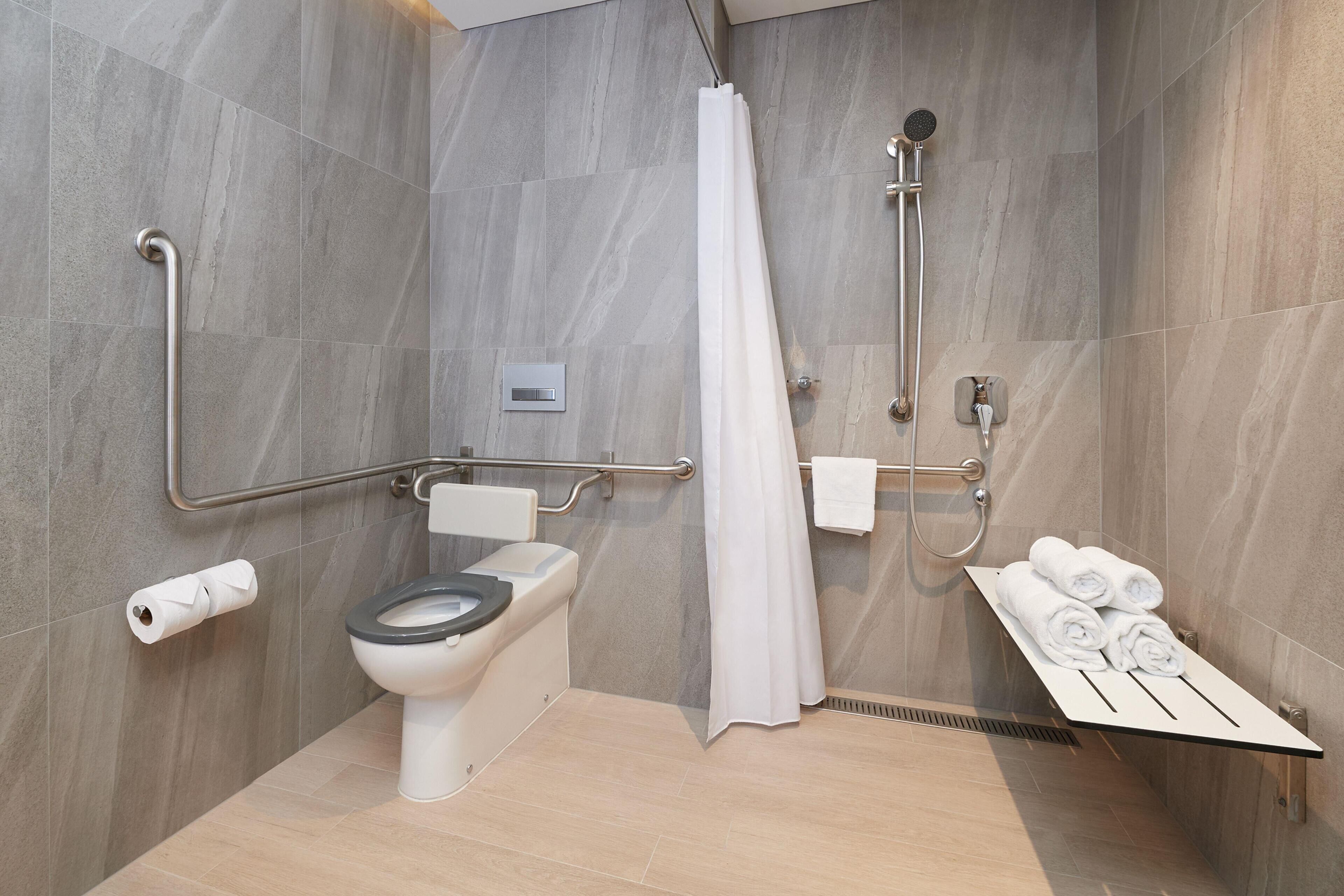 Un baño moderno con inodoro, ducha y barras de apoyo.